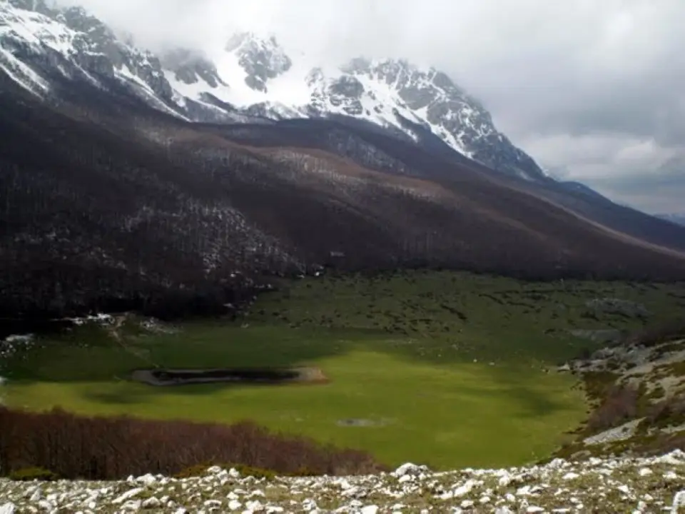 Un pianoro verde chiuso dalle cime innevate del parco Sirente-Velino.
