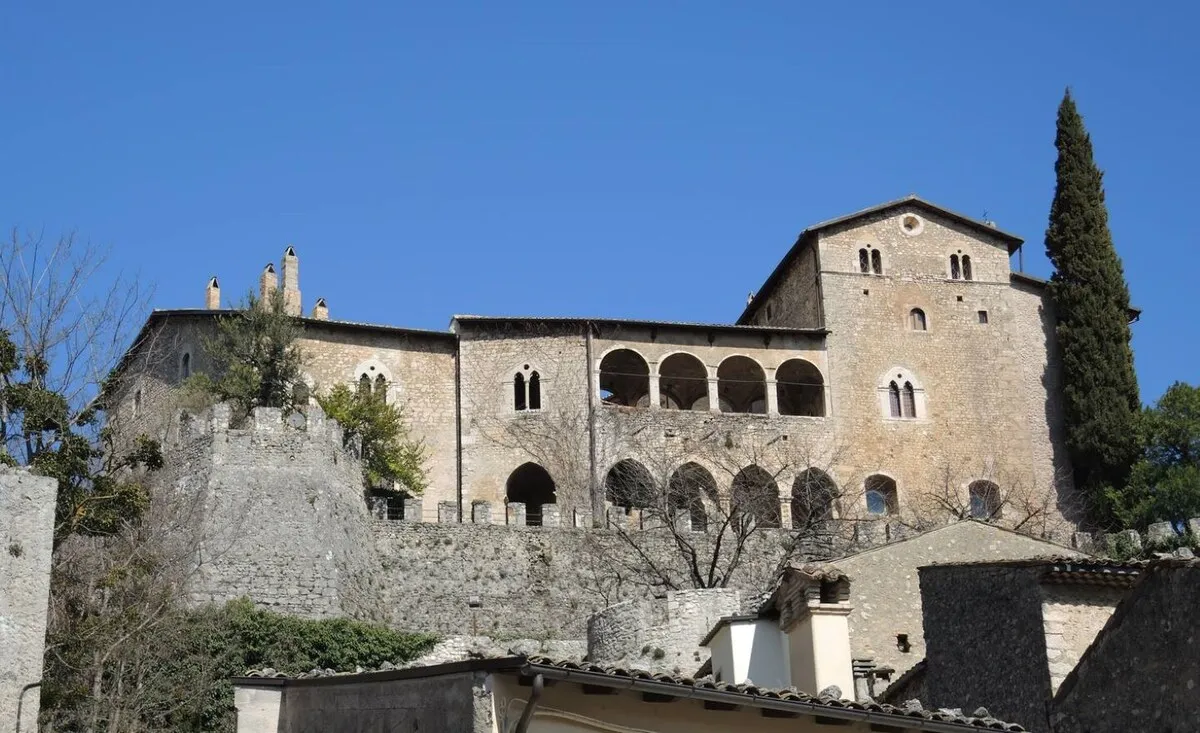 L’edificio storico in pietra che domina il borgo, con loggiato ad archi e cipresso.