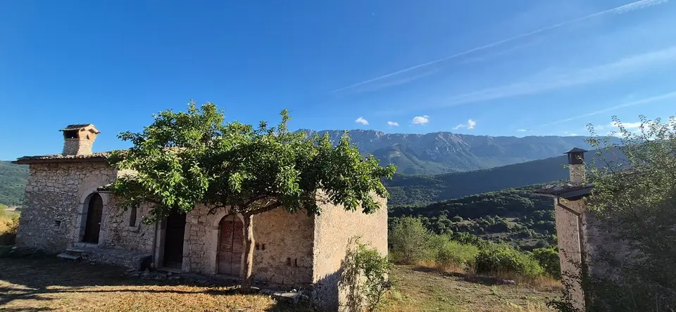 Piccola chiesa di pietra isolata sul crinale, con la valle e le montagne sullo sfondo.