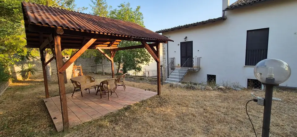Il pergolato in legno con tavolo e sedie nel giardino, accanto alla casa.