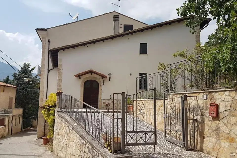 La facciata della villa, intonaco chiaro e basamento in pietra, con il cancello d’ingresso.