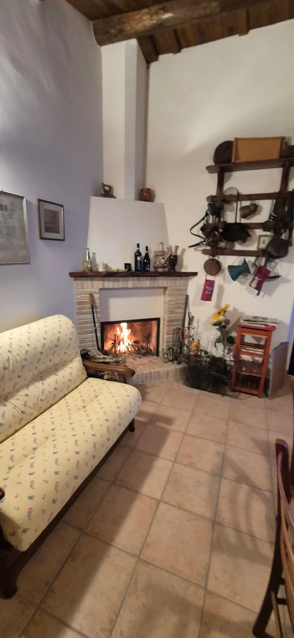 Il camino acceso nel soggiorno, con divano e pavimento in cotto.