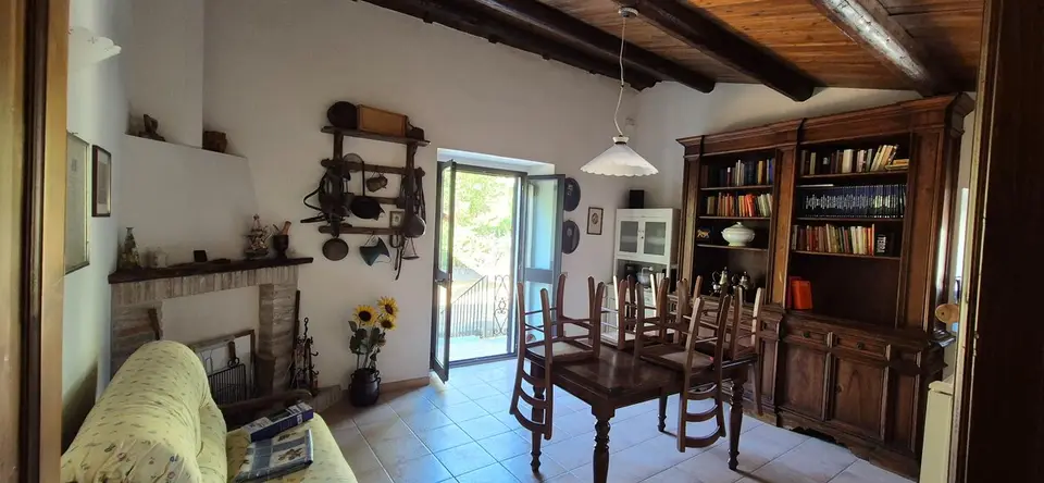La sala da pranzo con tavolo di legno, libreria e porta-finestra aperta sul giardino.